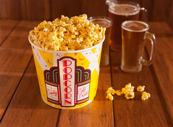 big tub of popcorn on a table next to two beers