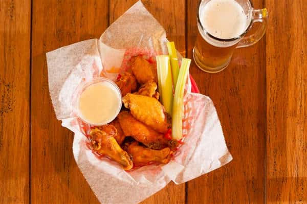 basket of wings with dipping sauce and celery with a glass of beer