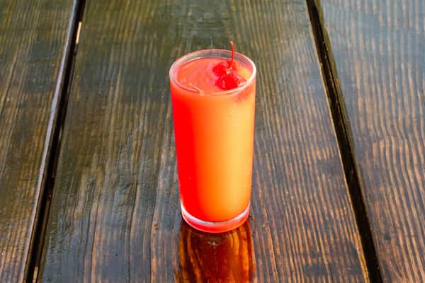 A vibrant tequila sunrise cocktail garnished with maraschino cherries on a rustic wooden table.