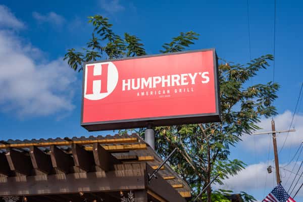 Bright red sign for Humphrey's American Grill, featuring a bold white "H" logo, set against a clear blue sky with tree branches.