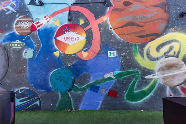 Vibrant space-themed mural featuring planets, rockets, and stars with "Humphrey's" at the center, painted on an outdoor wall.