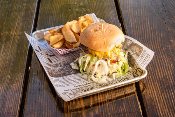 Cheeseburger with shredded lettuce, tomato, and melted cheese served with golden potato wedges on a rustic outdoor table.