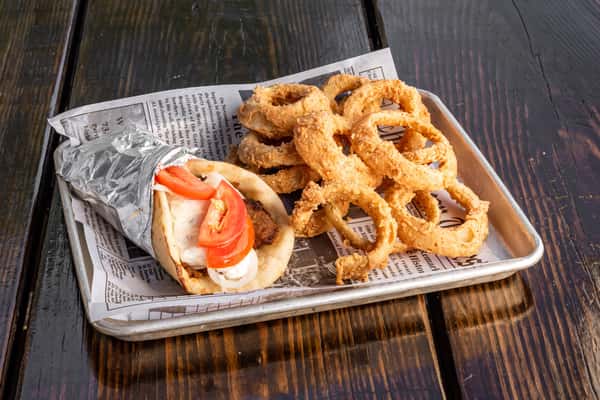 Gyro wrap with sliced tomato, onions, and tzatziki sauce in warm pita, served with a generous portion of crispy golden onion rings.