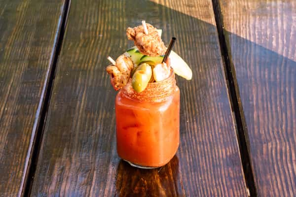 Bloody Mary garnished with skewers of fried chicken, shrimp, olives, cheese, cucumber, and a pickle spear in a mason jar.