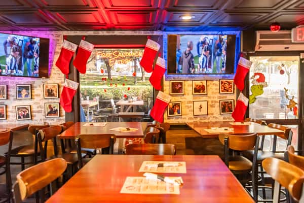 Festively decorated sports bar with Christmas stockings, TVs showing football, and cozy wooden tables set for dining.