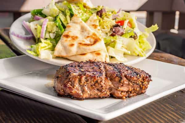 Juicy grilled filet steak served with a fresh Greek salad topped with feta, olives, pita wedges, and red onions.