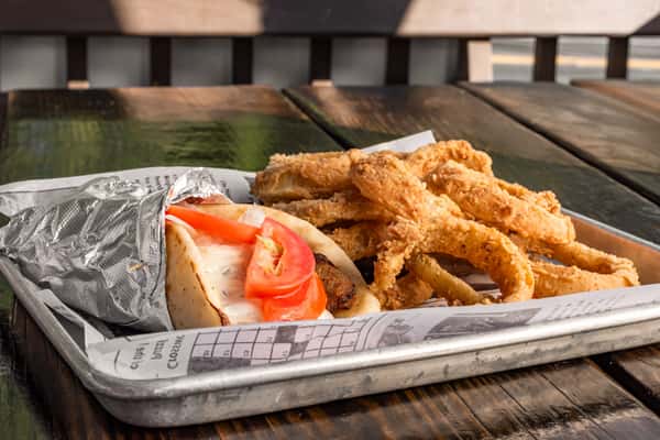 Lamb gyro wrapped in warm pita with tomato, onions, and tzatziki sauce, served with crispy battered onion rings on a metal tray.
