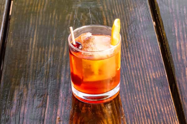 Classic old fashioned cocktail with a cherry and orange peel garnish on a rustic wooden table.