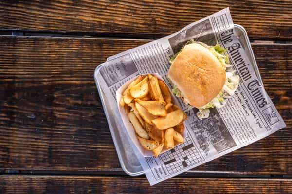 Classic chicken sandwich with lettuce served on a toasted bun, paired with thick-cut seasoned potato wedges on a metal tray.