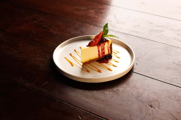 New York-style cheesecake with berry compote, caramel drizzle, and fresh mint garnish.