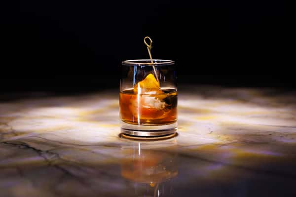 Classic Old Fashioned cocktail with orange garnish served over ice in a crystal rocks glass.