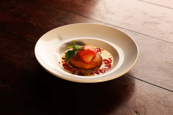 Strawberry shortcake-style dessert with fresh berries, whipped cream, and berry coulis served in a refined restaurant setting.