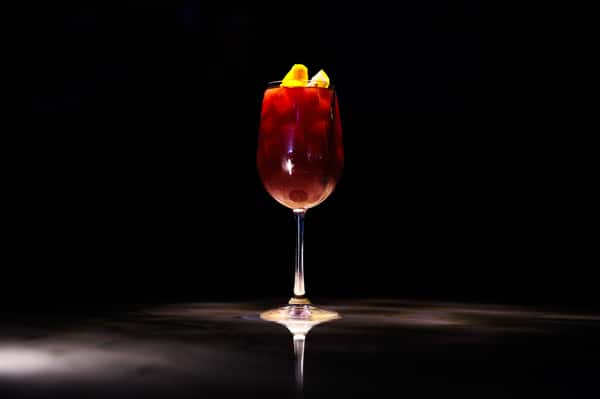 Refreshing berry cocktail garnished with citrus and fresh fruit in an elegant stemmed glass.
