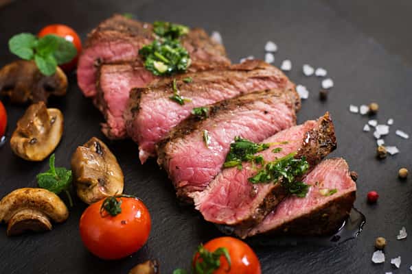 Sliced medium-rare steak with chimichurri, tomatoes, and mushrooms on a dark plate, a dish from City Limits Bar and Grill.