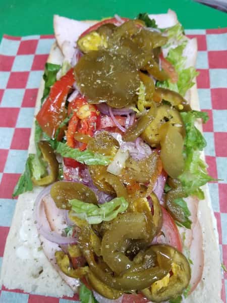 A cut open hero with peppers, vinaigrette, lettuce and red onion