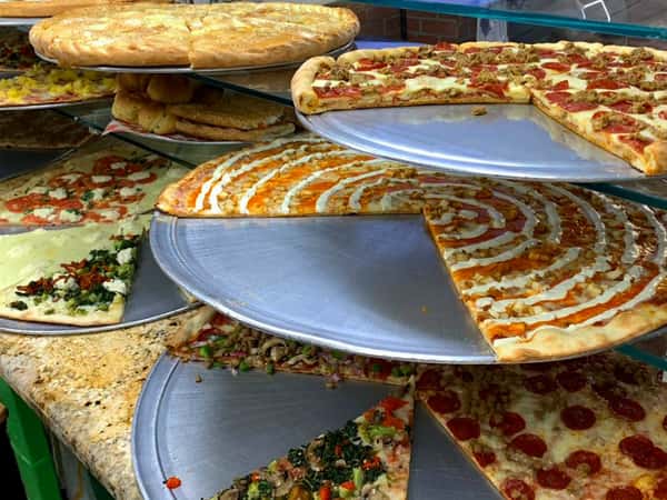 Many varieties of pizza pies placed on multiple elevated levels of pizza pans