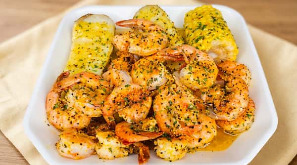 Shrimp boil with peeled shrimp, corn on the cob, and potatoes, all seasoned with herbs and spices.