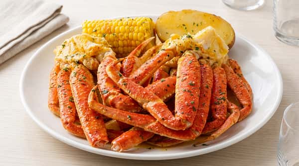 Snow crab legs with corn on the cob, potatoes and parsley, drizzled with butter sauce.