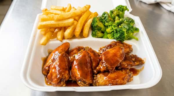 BBQ chicken wings, french fries, and broccoli in a white takeout container.