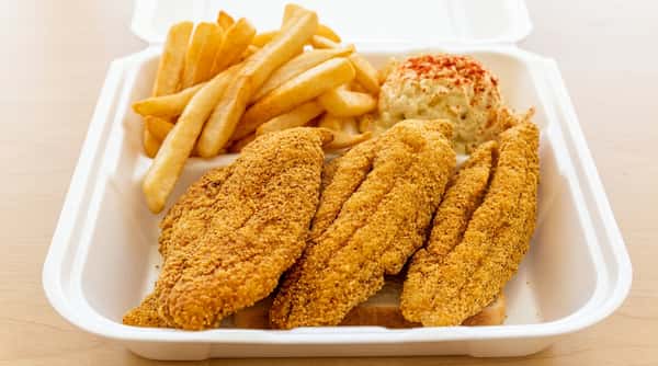 Fried catfish fillets with french fries and a scoop of potato salad sprinkled with paprika, served in a white to-go container.