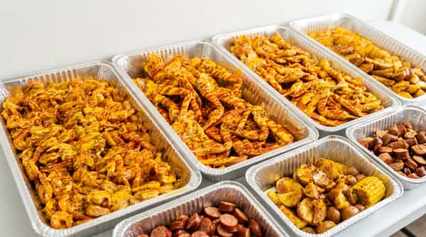 Multiple aluminum trays filled with bright orange seafood (shrimp and lobster tails) coated in a yellow sauce.