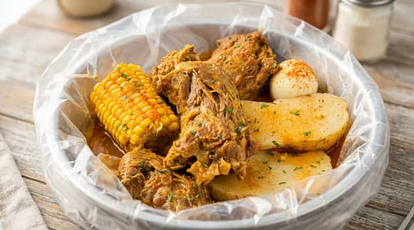 Stew with corn on the cob, dark meat, potato, and a hard-boiled egg with paprika.