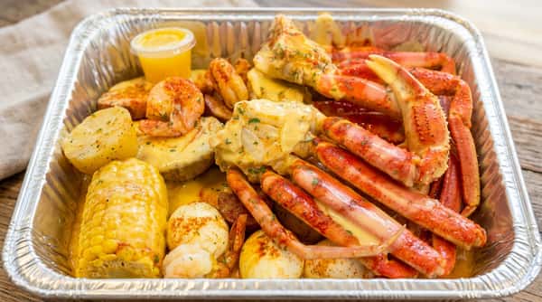 Seafood boil with crab legs, shrimp, potatoes, corn, and eggs, all topped with a yellow sauce and spices.