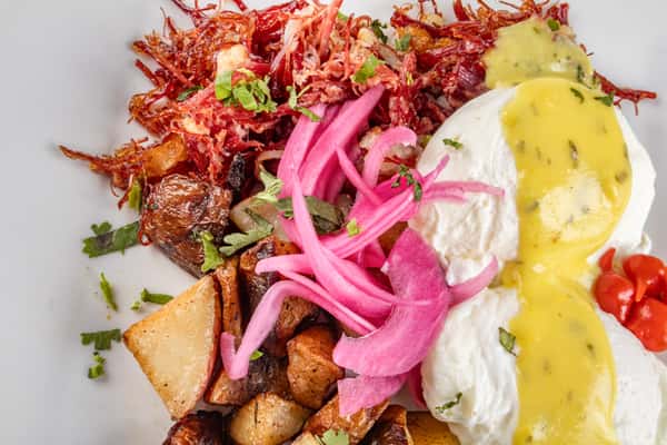 Savory corned beef hash with poached eggs, hollandaise sauce, pickled red onions, and crispy roasted potatoes, garnished with fresh herbs for a comforting brunch dish.