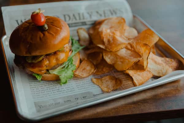 Juicy Irish pub cheeseburger with lettuce and melted cheese, served on a toasted bun with house-made potato chips on newspaper-lined tray.