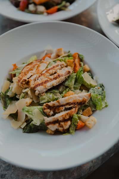 Grilled chicken Caesar-style salad with romaine lettuce, shaved parmesan, croutons, and creamy dressing, served in a white bowl at an Irish pub restaurant