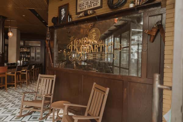 Vintage Irish pub interior with wooden rocking chairs, patterned tile floor, and a glass partition displaying The Henry McCarty Irish Pub name, creating a warm, old-world bar atmosphere.