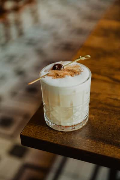 Creamy Irish whiskey cocktail topped with foam, cocoa dust, and cherry garnish, served in a rocks glass on a pub table.