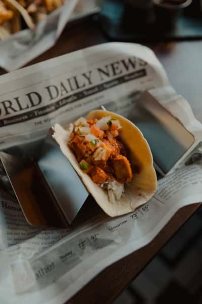 Soft taco filled with seasoned meat, diced onions, and herbs, served on newspaper-style liner at a pub restaurant