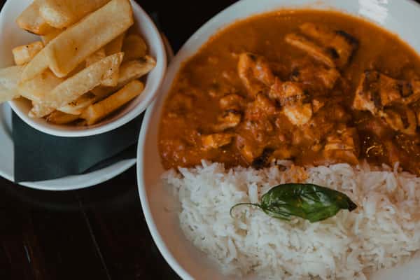 Irish-style curry with tender chicken pieces served over white rice, garnished with fresh basil and paired with thick-cut fries.