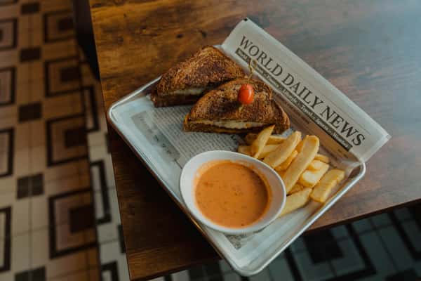 Grilled pub sandwich served with thick-cut fries and a side of creamy dipping sauce on a newspaper-lined tray.