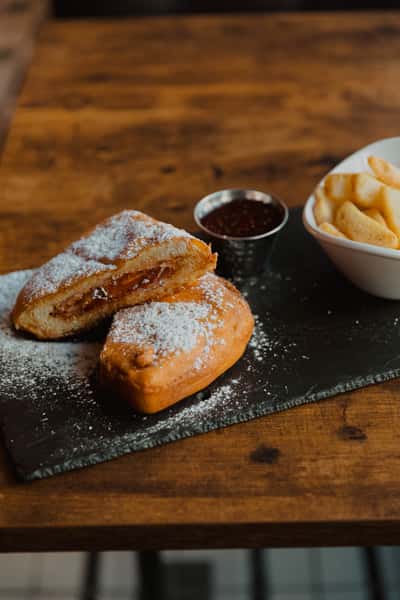Golden fried pastry dusted with powdered sugar, served with dipping sauce and kettle chips on a slate board.