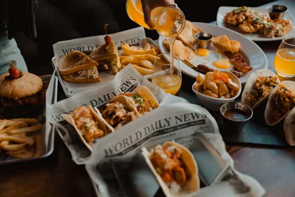 Irish pub brunch spread featuring tacos, sandwiches, burgers, fries, breakfast plates, and mimosas shared across a wooden table.