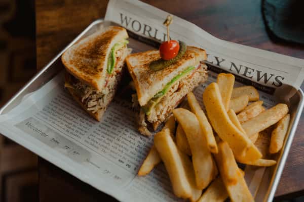 Toasted turkey sandwich layered with greens and cheese, served with thick-cut fries on a newspaper-lined pub tray