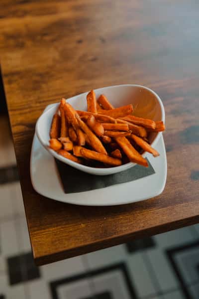 Bowl of crispy sweet potato fries served on a small plate atop a wooden table in a casual Irish pub setting