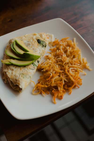 Savory omelet topped with fresh avocado slices, served with crispy shredded hash browns on a white plate.