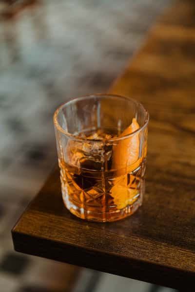 Glass of amber whiskey on the rocks with citrus peel garnish, served on a wooden table inside a classic Irish pub.