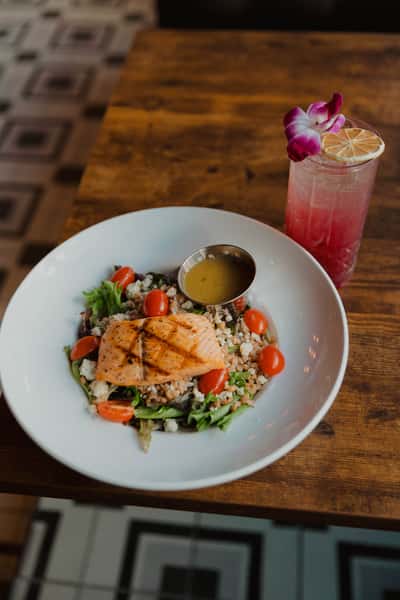 Grilled salmon salad with mixed greens, grains, cherry tomatoes, and house dressing, paired with a pink craft cocktail at an Irish pub.