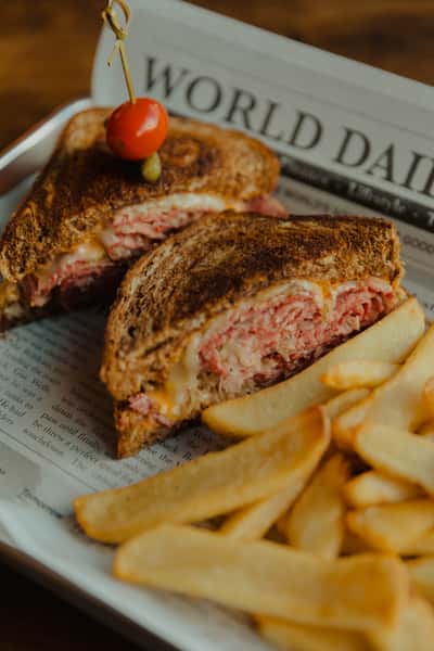 Grilled corned beef sandwich with melted cheese, served with thick-cut fries on a newspaper-lined tray at an Irish pub.