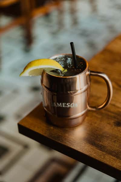 Jameson whiskey cocktail served in a metal mug with crushed ice, lemon wedge, and black straw on a wooden pub table