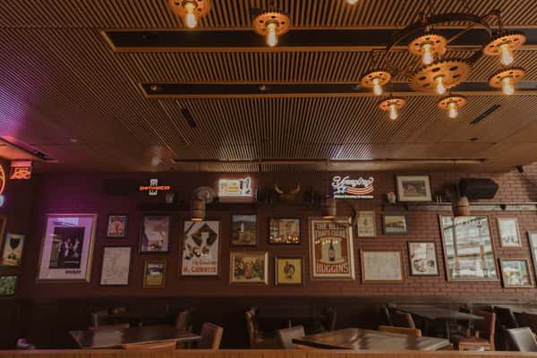 Cozy Irish pub dining room with framed vintage posters, exposed brick walls, and warm industrial lighting that creates a classic neighborhood pub vibe.