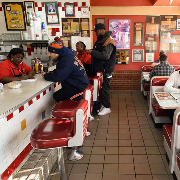Customers seated at a classic red-and-white diner counter while staff take orders in a retro restaurant interior.