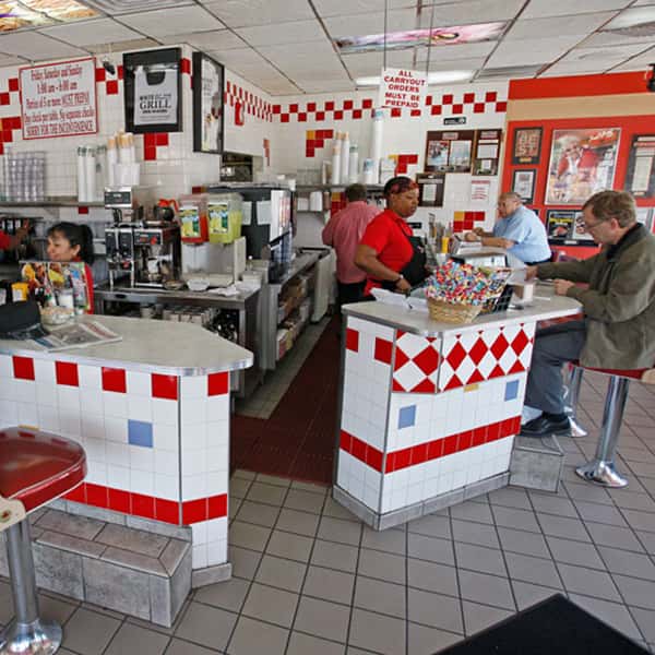 Classic diner counter interior with red and white tile, staff preparing orders, and customers seated at the bar.