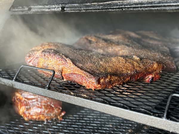 A close-up shot of brisket smoking in a smoker, with a rich bark forming on the meat and smoke swirling around.