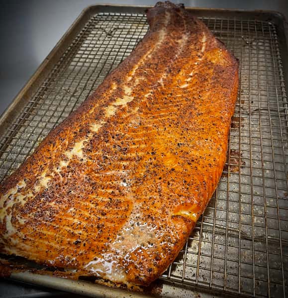 A seasoned slab of salmon on a wire rack, ready to be cooked or smoked, showcasing a beautifully crispy, caramelized exterior.