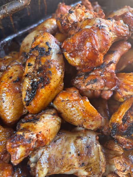 A close-up shot of freshly grilled chicken wings with a golden-brown, crispy exterior, showing some charred areas, likely cooked on a barbecue.